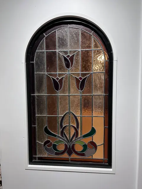 Arched stained glass insert with a floral design, installed in a white wall